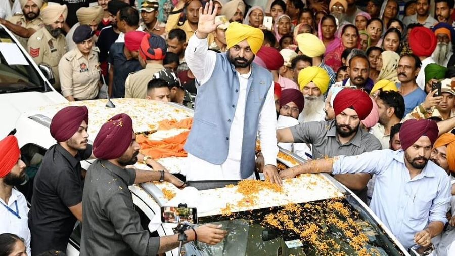 Punjab Chief Minister Bhagwant Mann waves to supporters during a large public gathering, surrounded by security personnel and crowds.